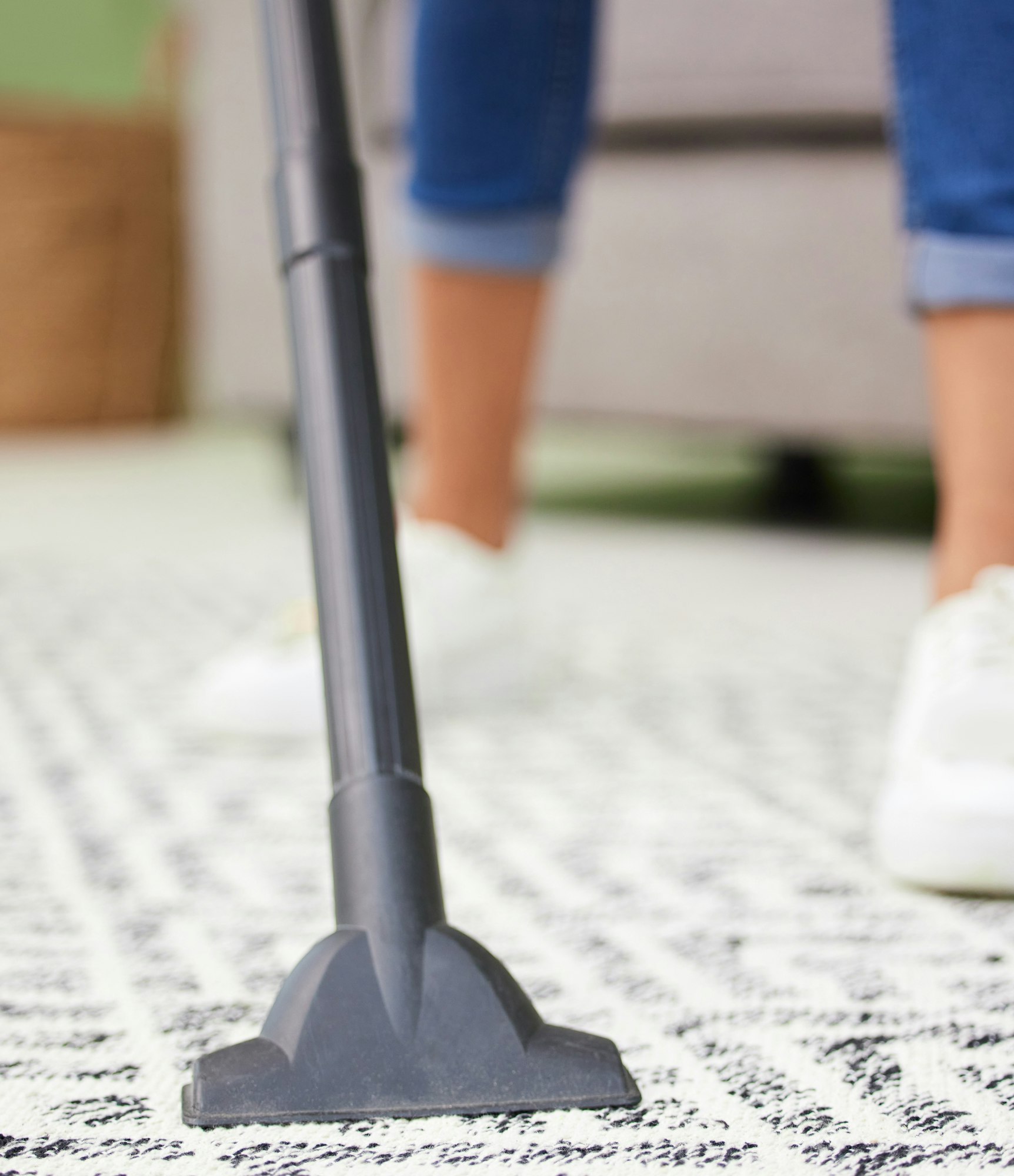 Cropped shot of an unrecognizable woman standing and using a vacuum to clean her carpet at home